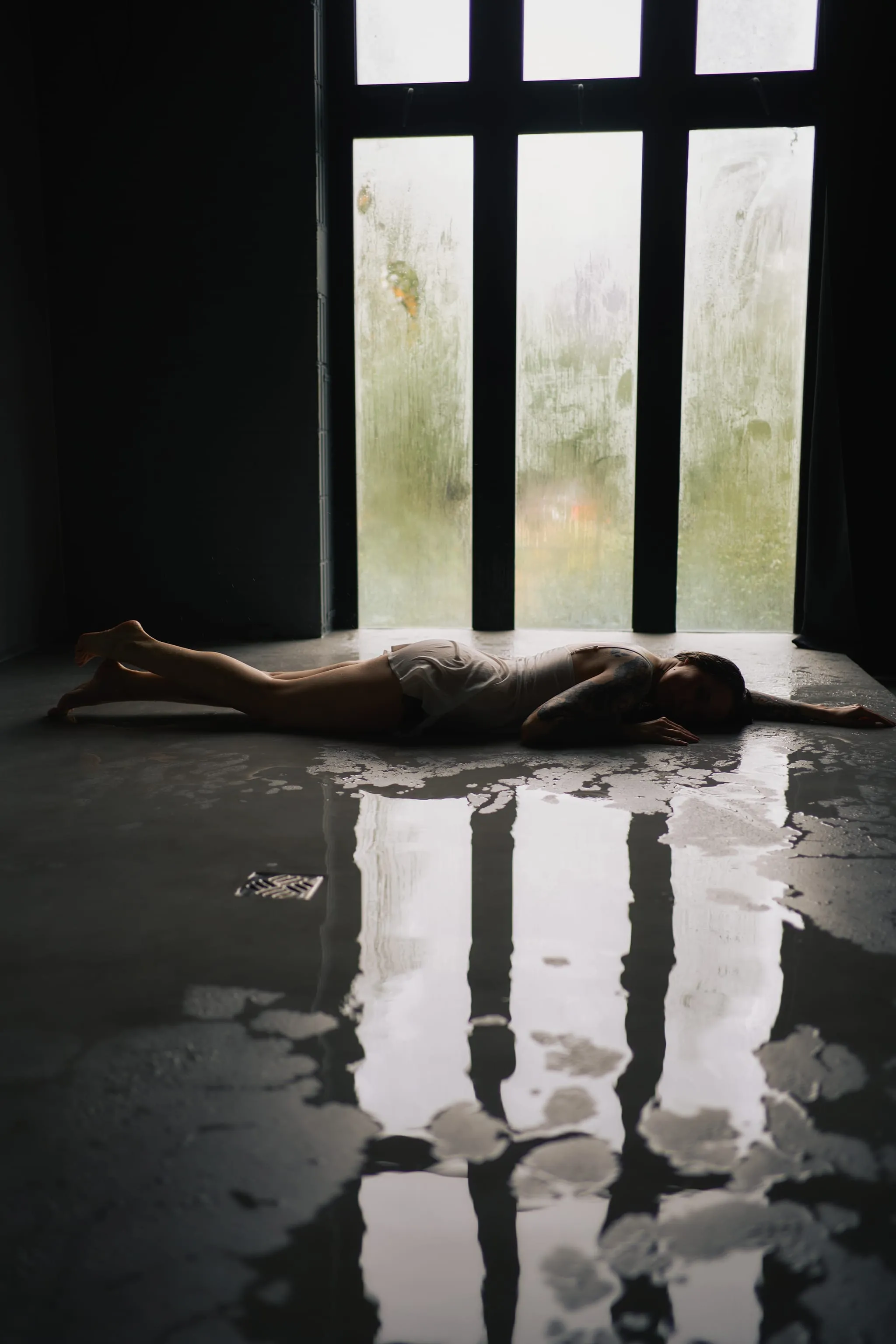 Kobieta leżąca przy wysokim oknie, światło odbite w wodzie na podłodze - fotografia kobieca