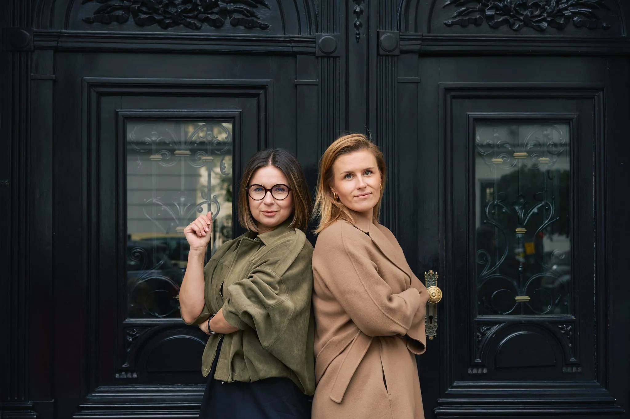 Dwie kobiety stojące plecami do siebie przed zdobnymi czarnymi drzwiami - fotografia wizerunkowa