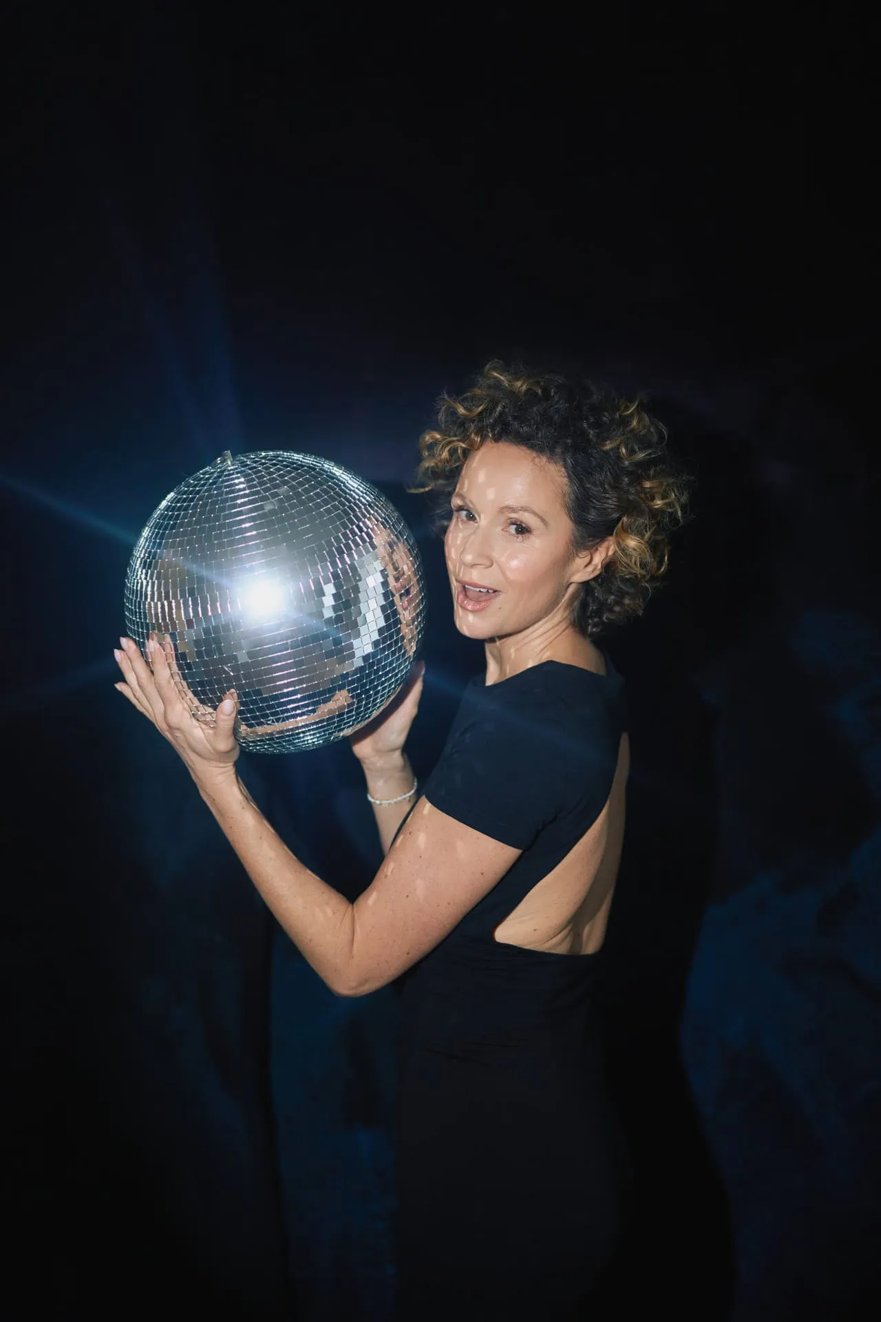 Aktorka z lustrzaną kulą disco w czarnej sukni z odkrytymi plecami