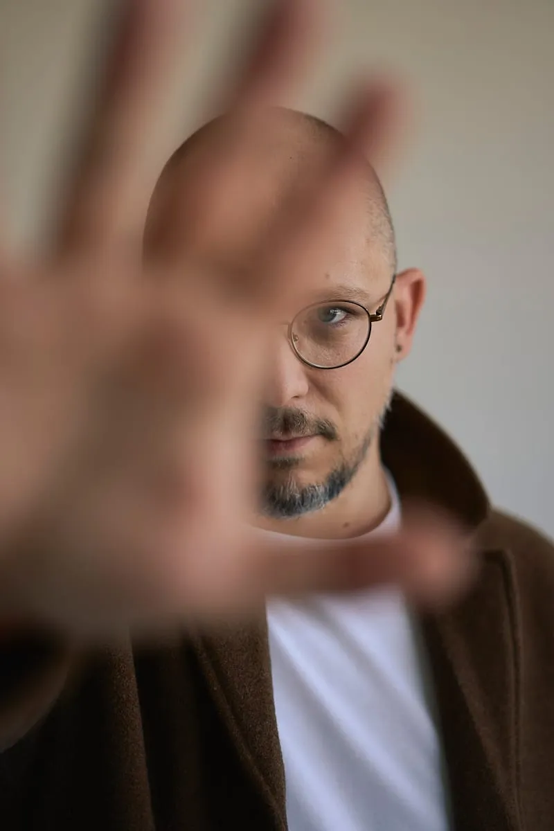 Mężczyzna zasłaniający obiektyw dłonią, portret w studiu