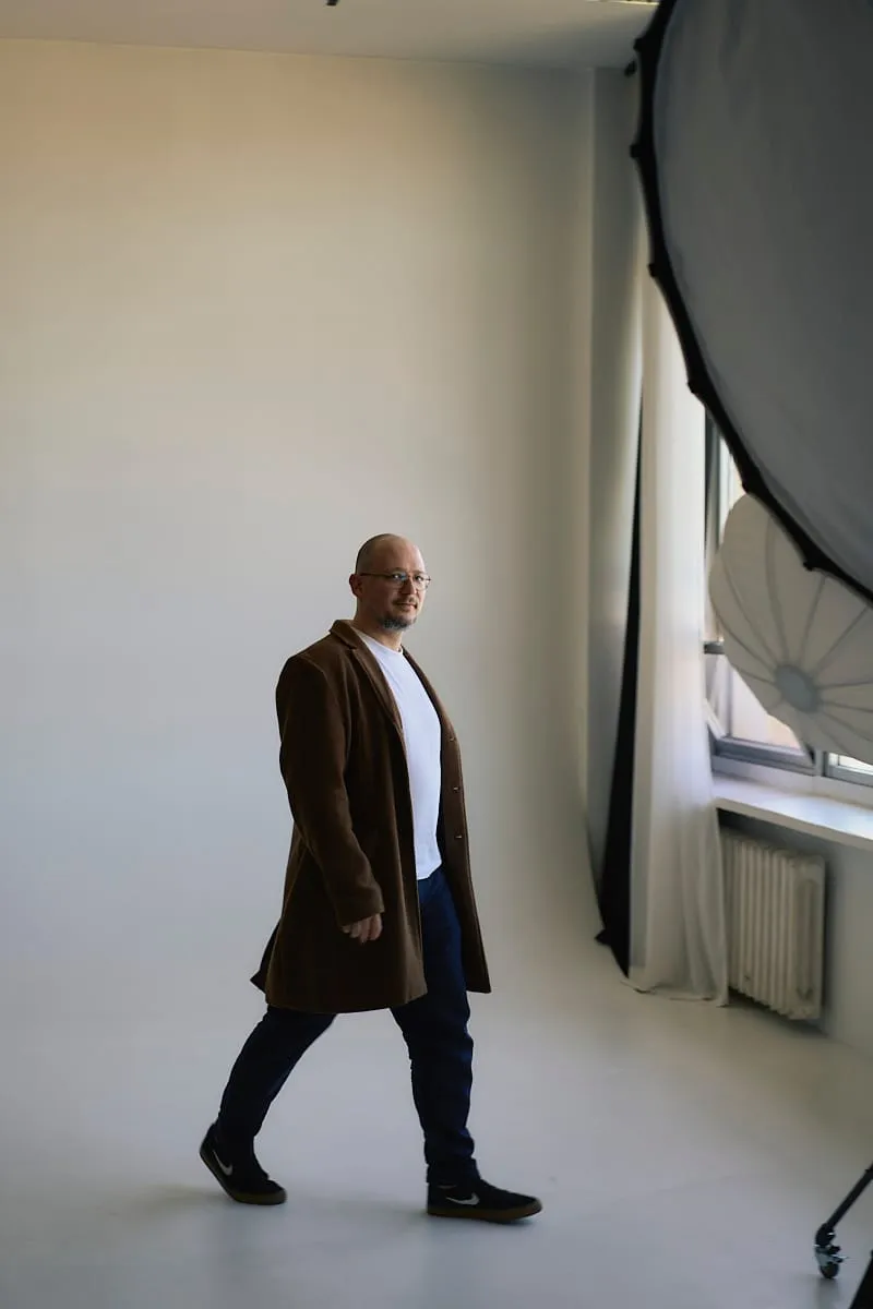 Mężczyzna w brązowym płaszczu przechodzący przez studio
