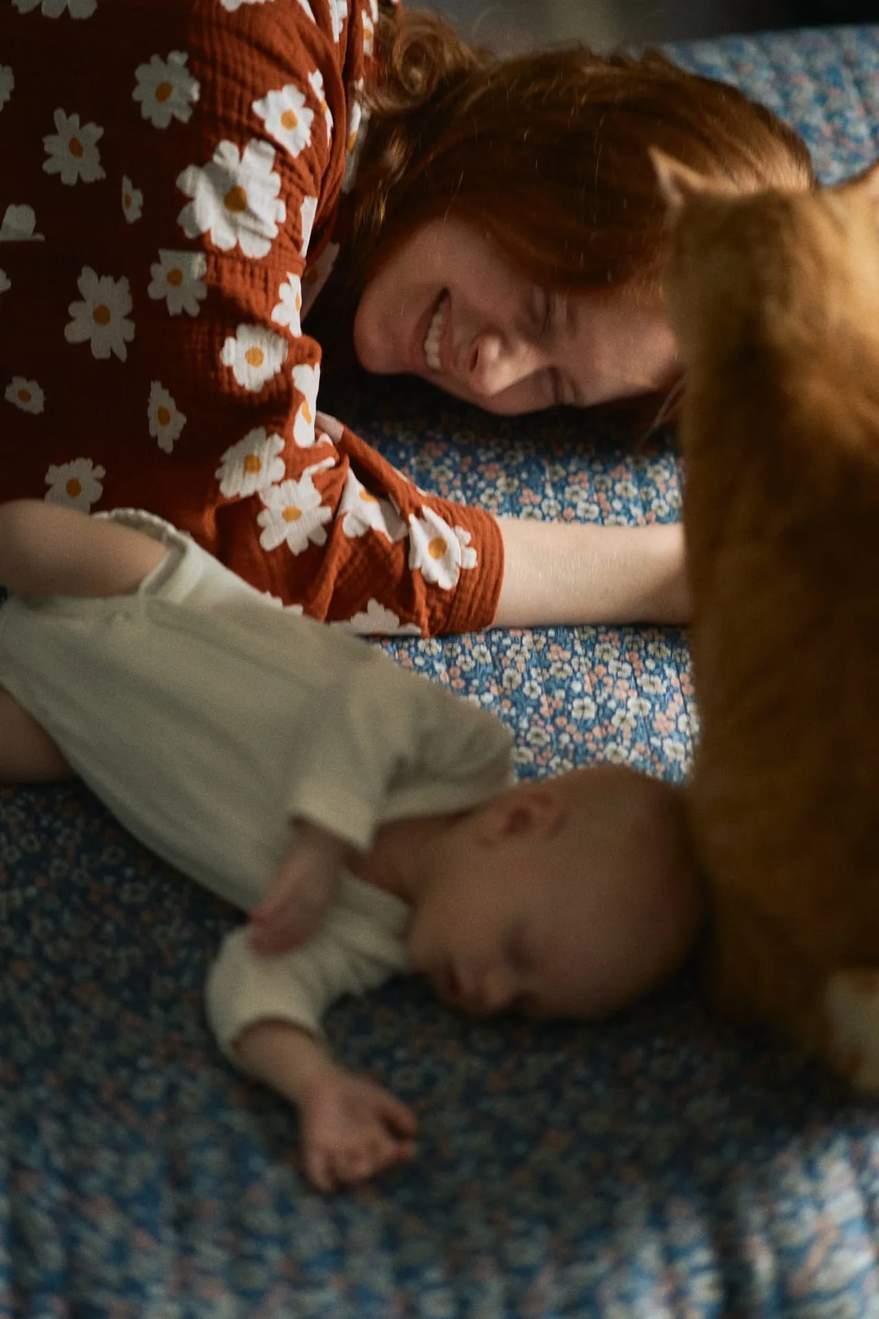 Mama i niemowlę na łóżku, obok rudy kot